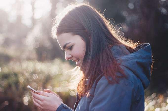 Nuori nainen katsoo hymyillen puhelintaan ollessaan kävelyllä luonnossa.