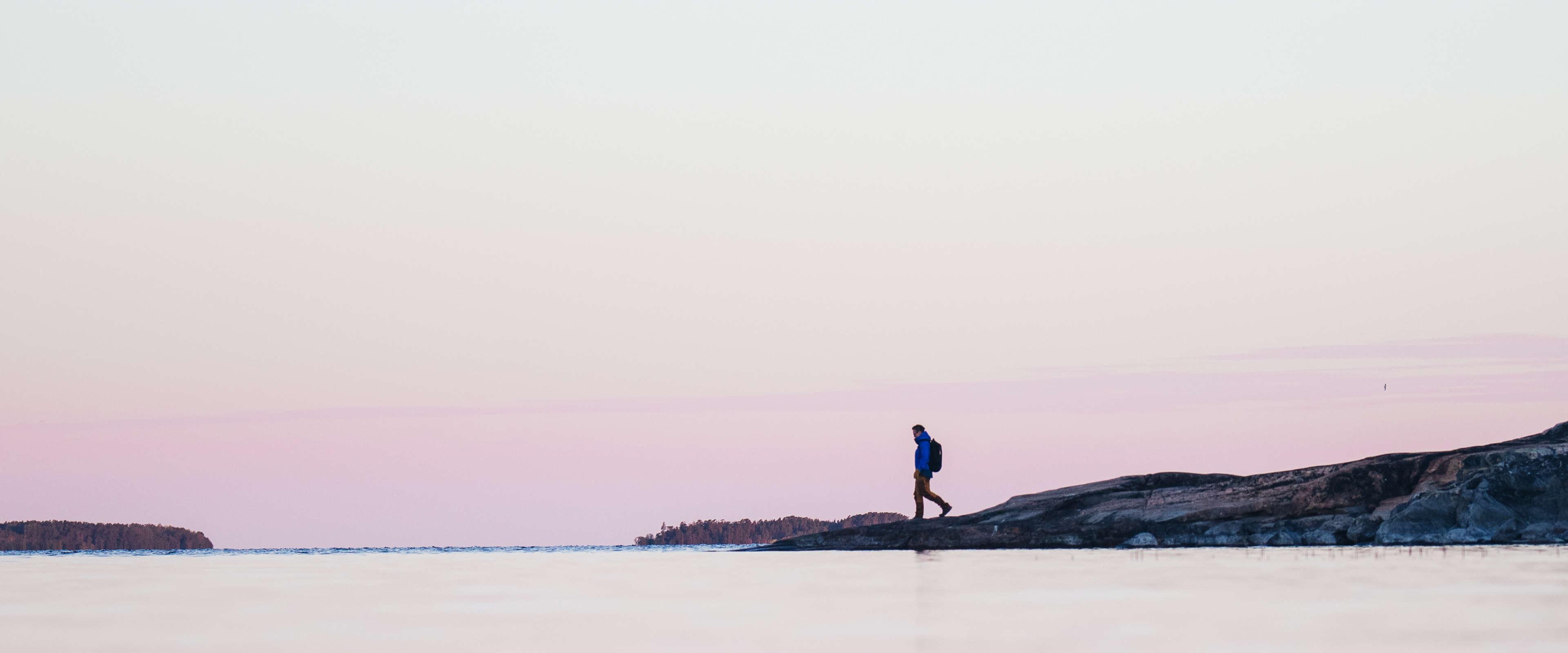 Poutapilven työntekijä vaeltaa kallioisella rannalla auringon noustessa.