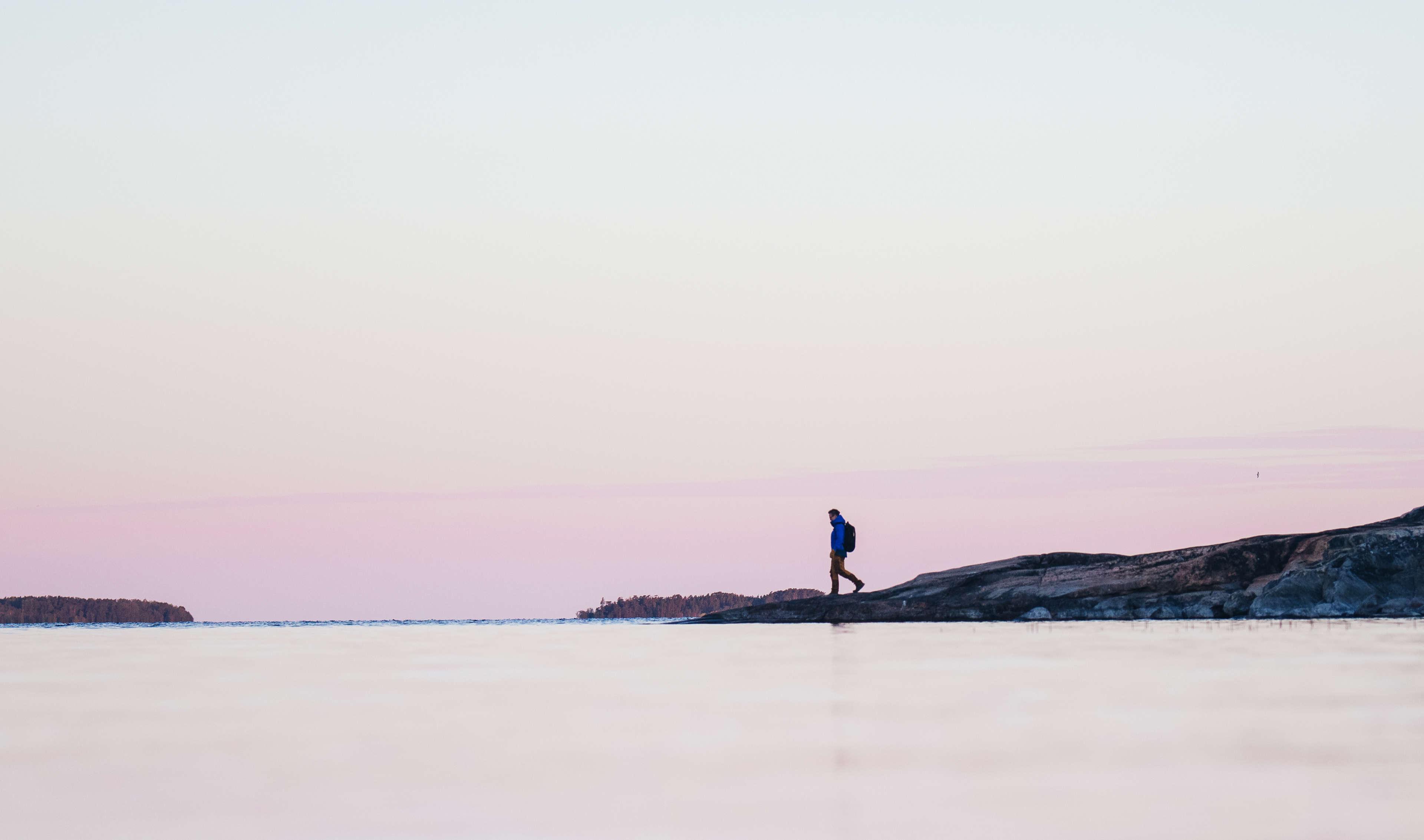 Poutapilven työntekijä vaeltaa kallioisella rannalla auringon noustessa.