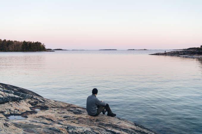 Poutapilven työntekijä istuu kalliolla meren äärellä katsellen kaukaisuuteen.